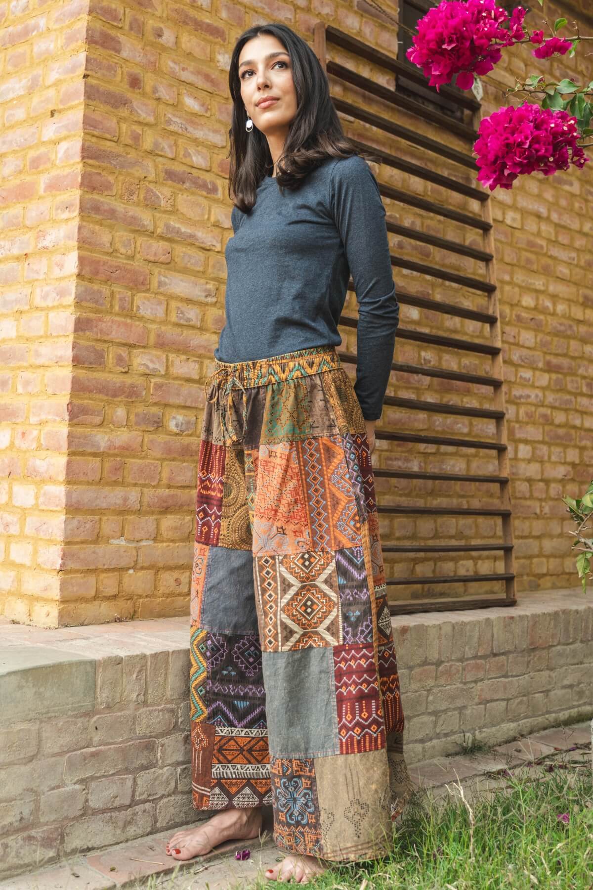 Woman standing near a building wearing colourful patchwork pants with elastic waist and a plain organic cotton long sleeve top.