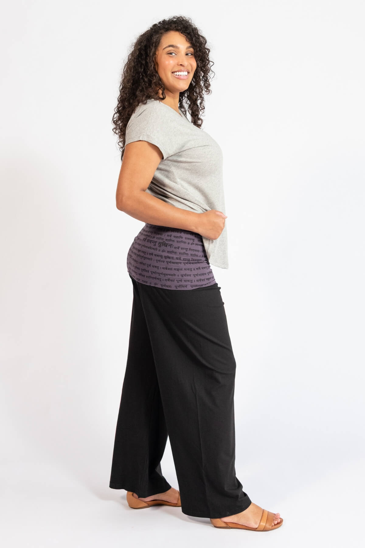 Woman wearing black turn over waist pants, turned to the right and against a white background