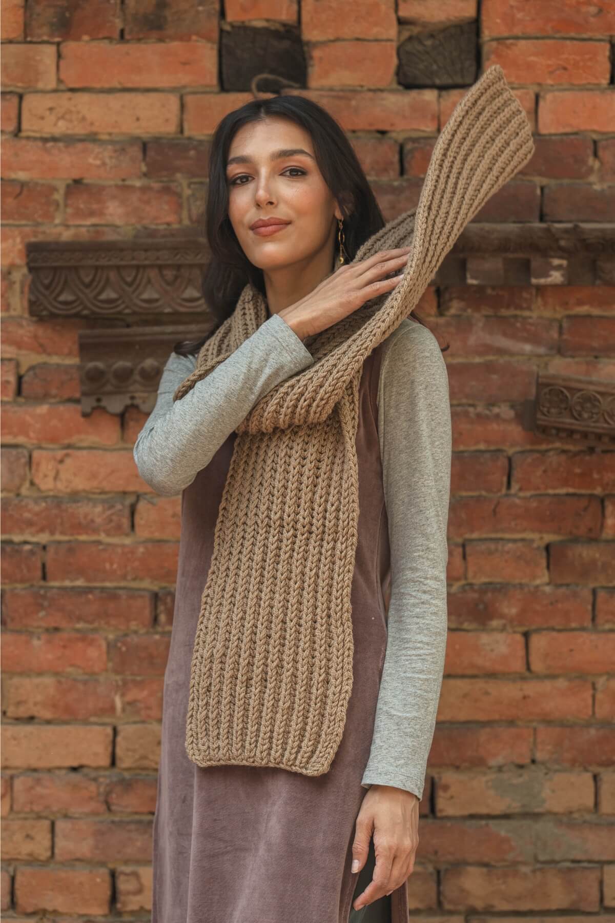 Woman wearing a beige knitted scarf against a brick wall