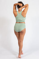 Person wearing a green sports bra and high-waisted briefs on a white background