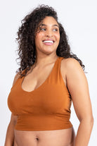 Woman wearing a caramel-colored tank top against a white background