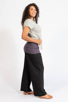 Woman wearing black turn over waist pants, turned to the right and against a white background