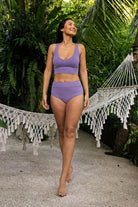 Woman standing near a hammock in a tropical garden, wearing lilac purple organic cotton bralette and high waist panties. 