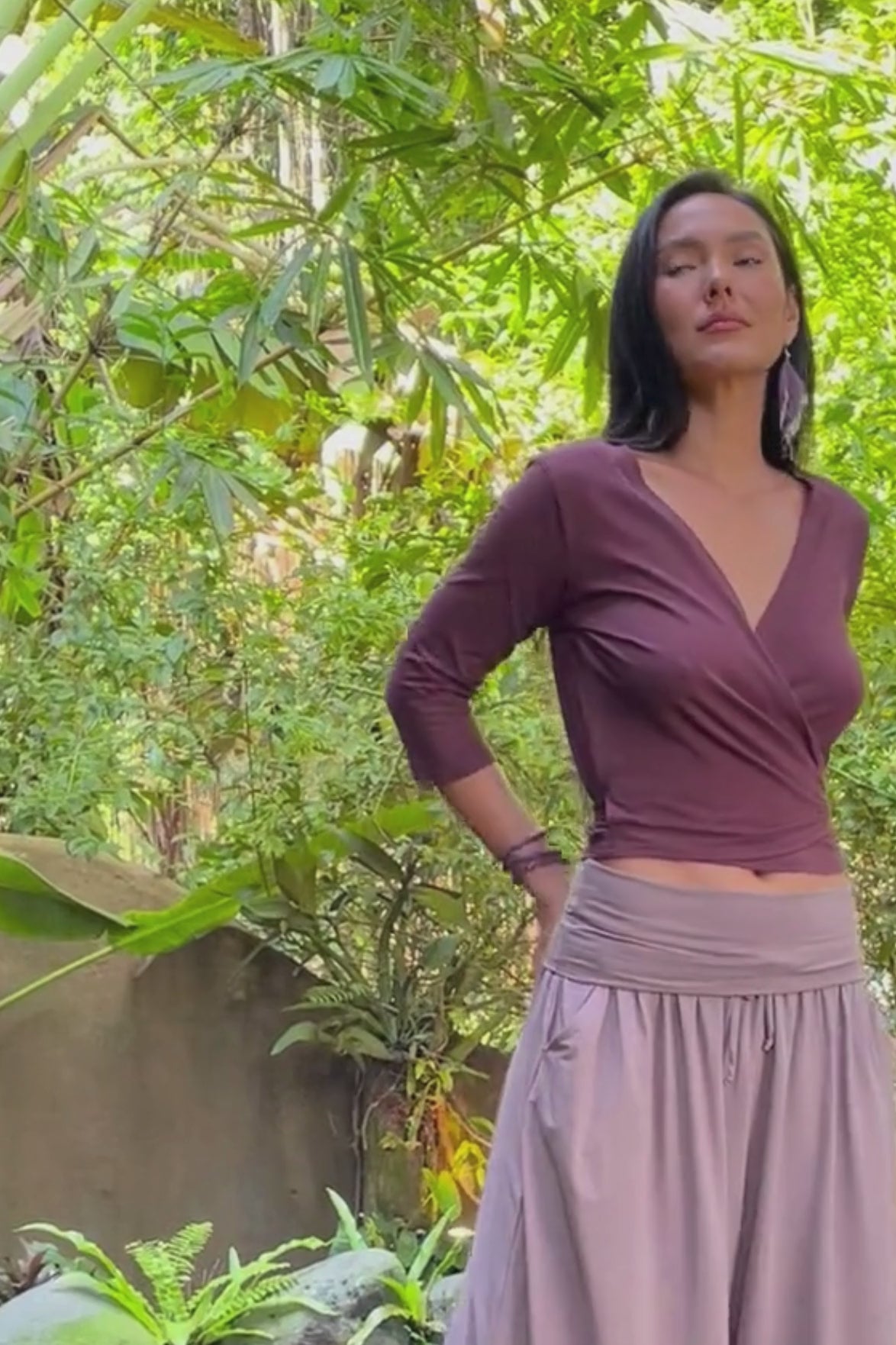 Woman wearing an organic cotton wrap top with wide leg turndown waist pants in a lush green jungle.