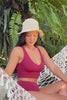 Woman sitting on a hammock surrounded by jungle, wearing a red bikini and a crochet hemp hat.